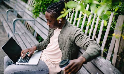 Man sitting on a bench searching on his laptop